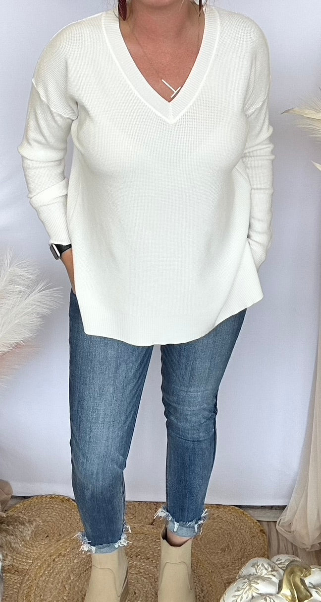 Person wearing a white sweater and blue jeans against a plain background