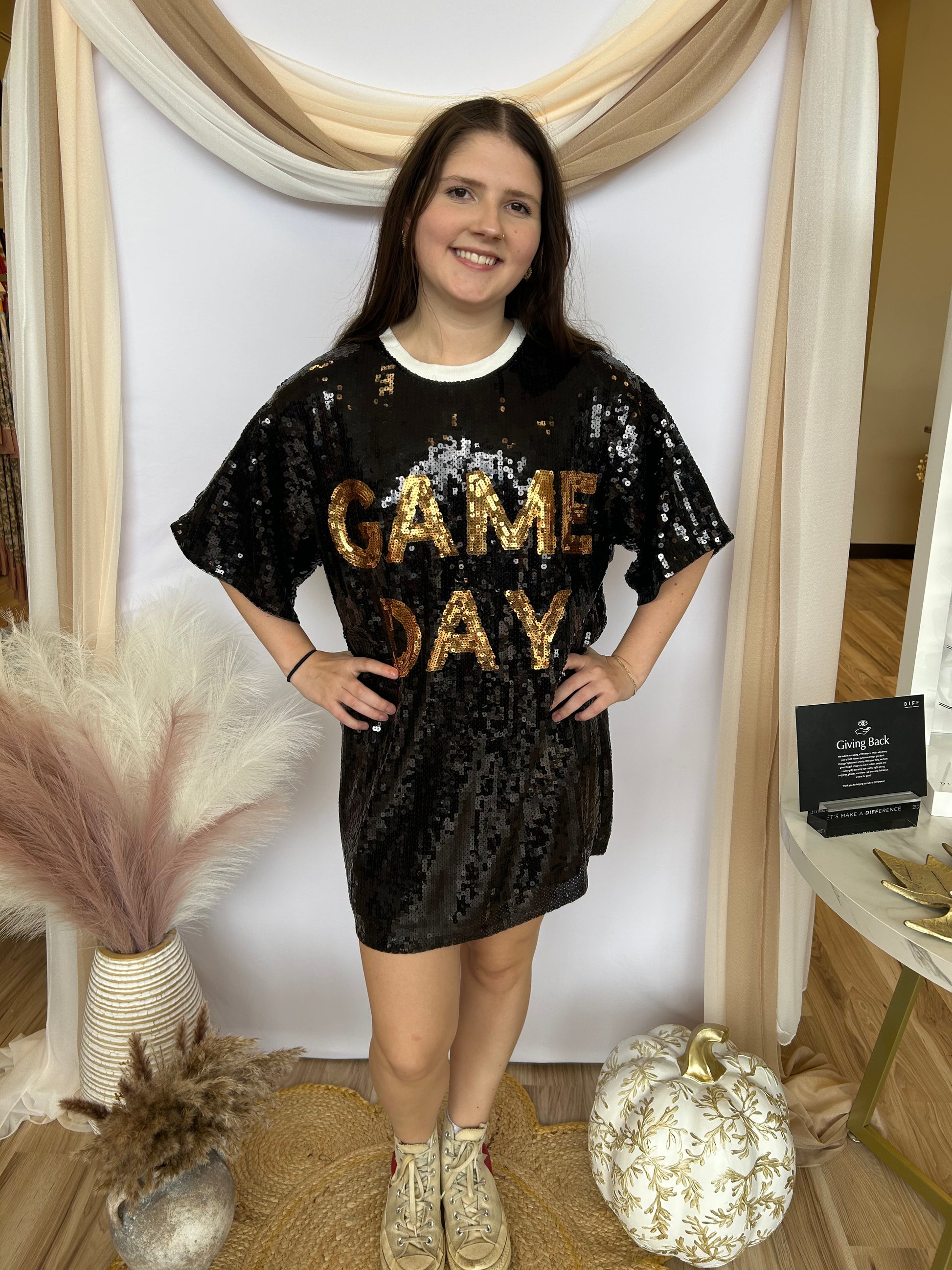 Woman wearing a black sequin dress with 'GAME DAY' text in a decorated indoor setting.