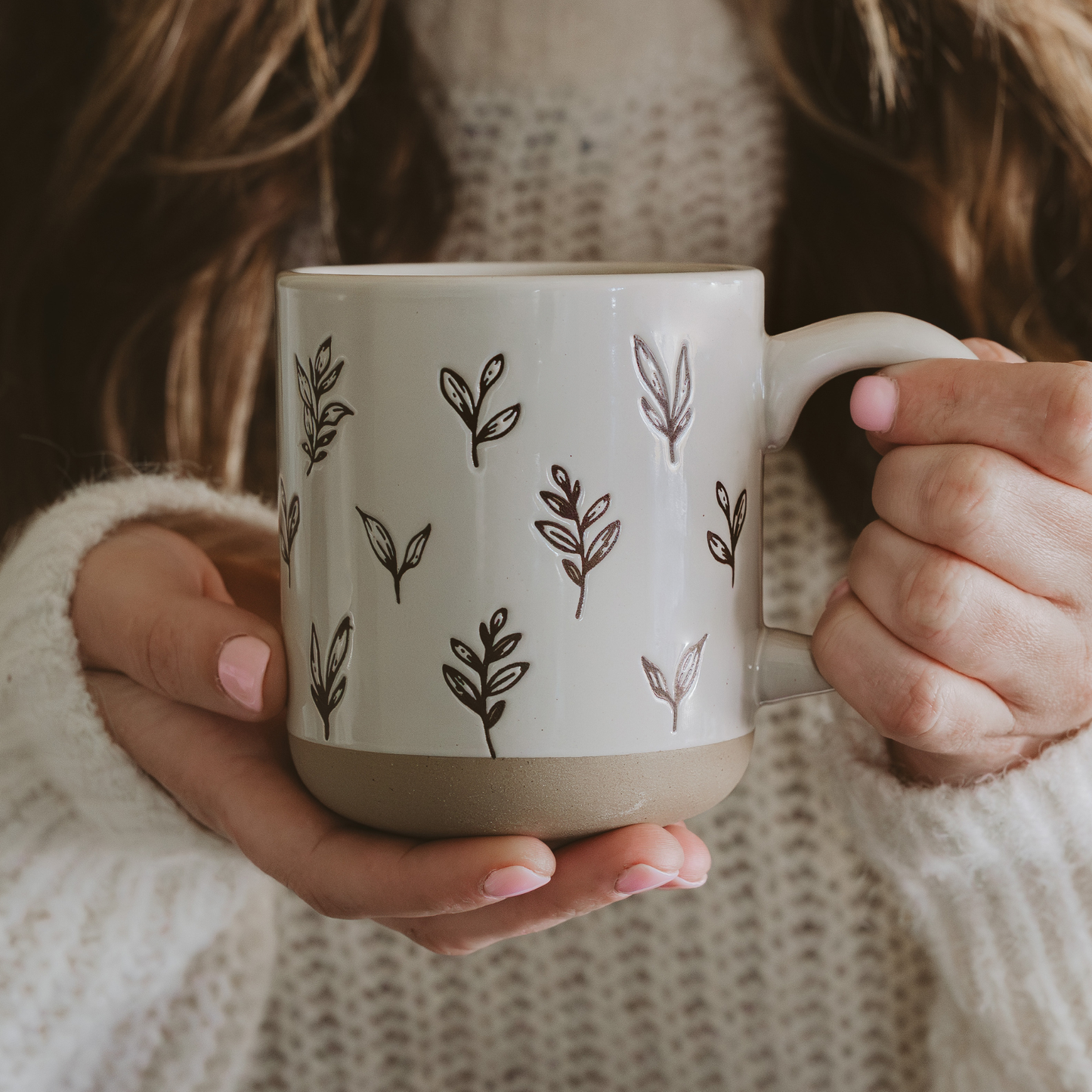 Person holding a mug with leaf patterns against a neutral background