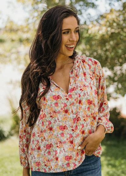 Woman wearing a floral blouse outdoors with greenery in the background