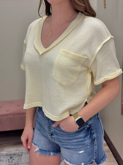 Person wearing a yellow textured top with a pocket and denim shorts indoors.