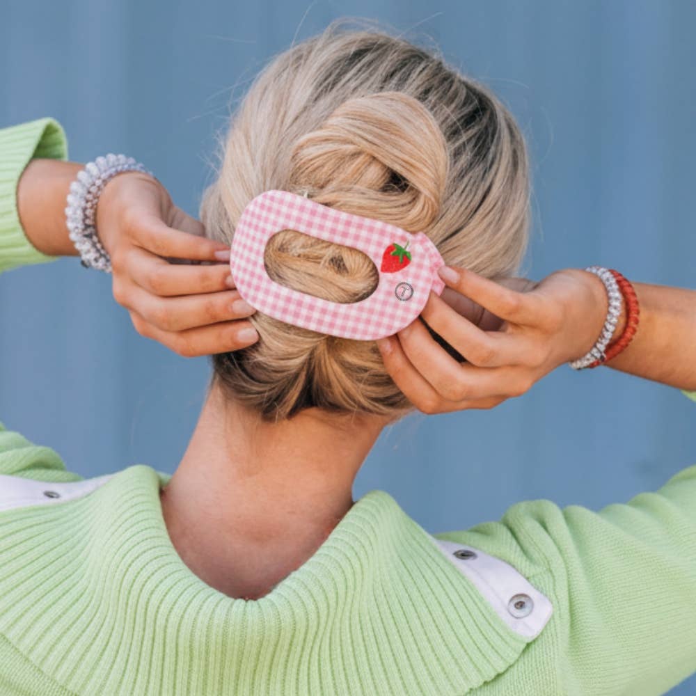 Person wearing a green sweater with a pink checkered hair tie featuring a sloth design against a blue background.