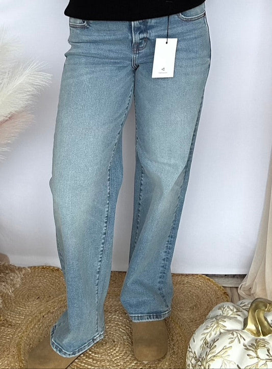 Person wearing a black sweater and light blue jeans with a tag, standing against a white background.