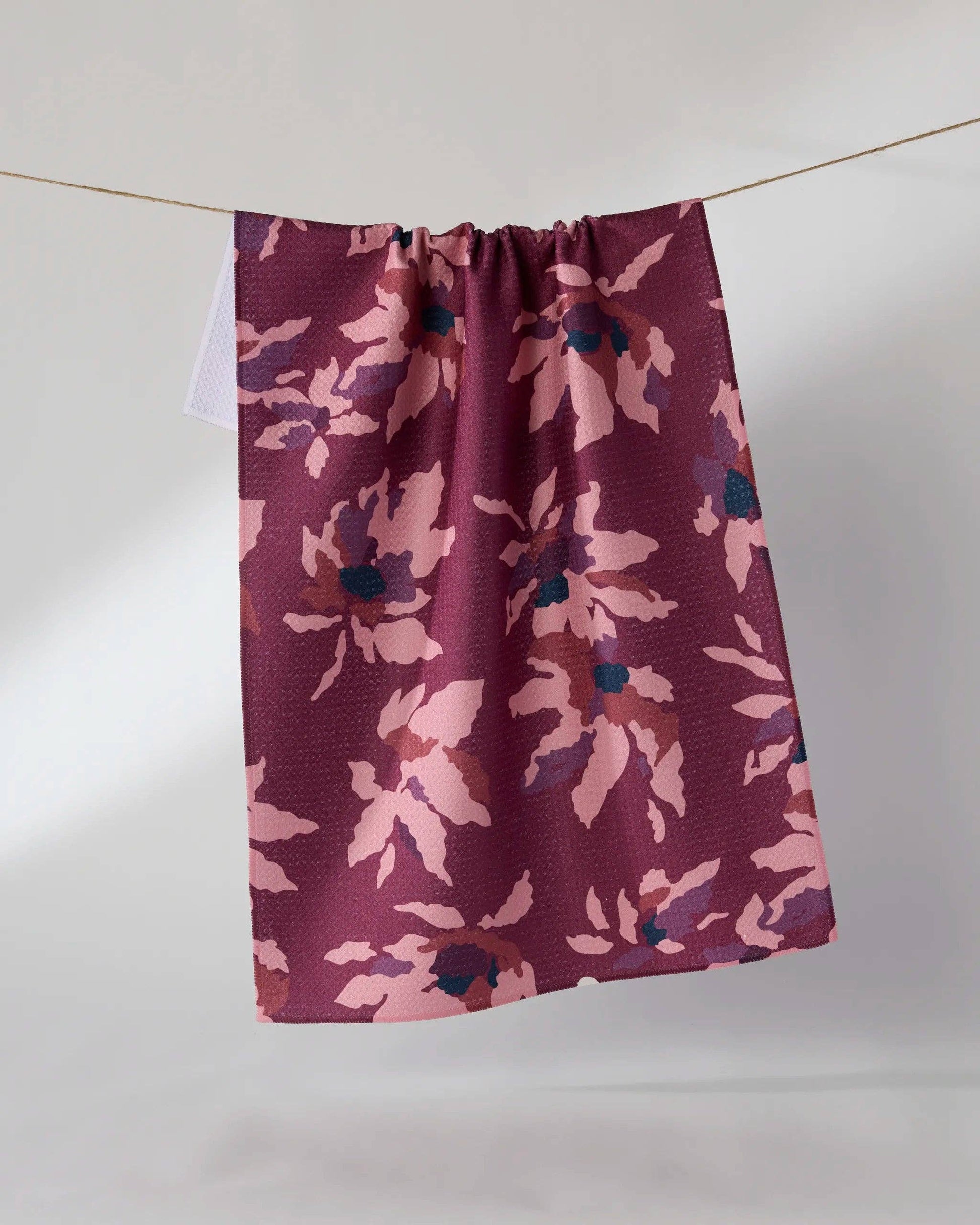 A single fabric curtain panel hanging from a thin cord against a plain light gray wall. The curtain has a waffle texture and features a floral pattern in dusty pink, mauve, and dark navy blue.