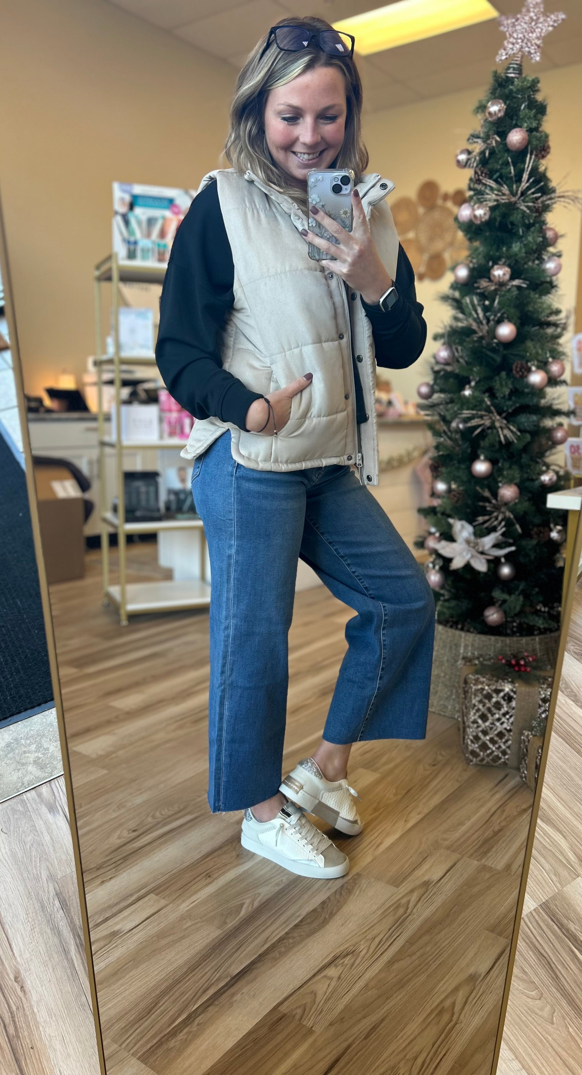 Woman taking a mirror selfie in a store with a Christmas tree in the background