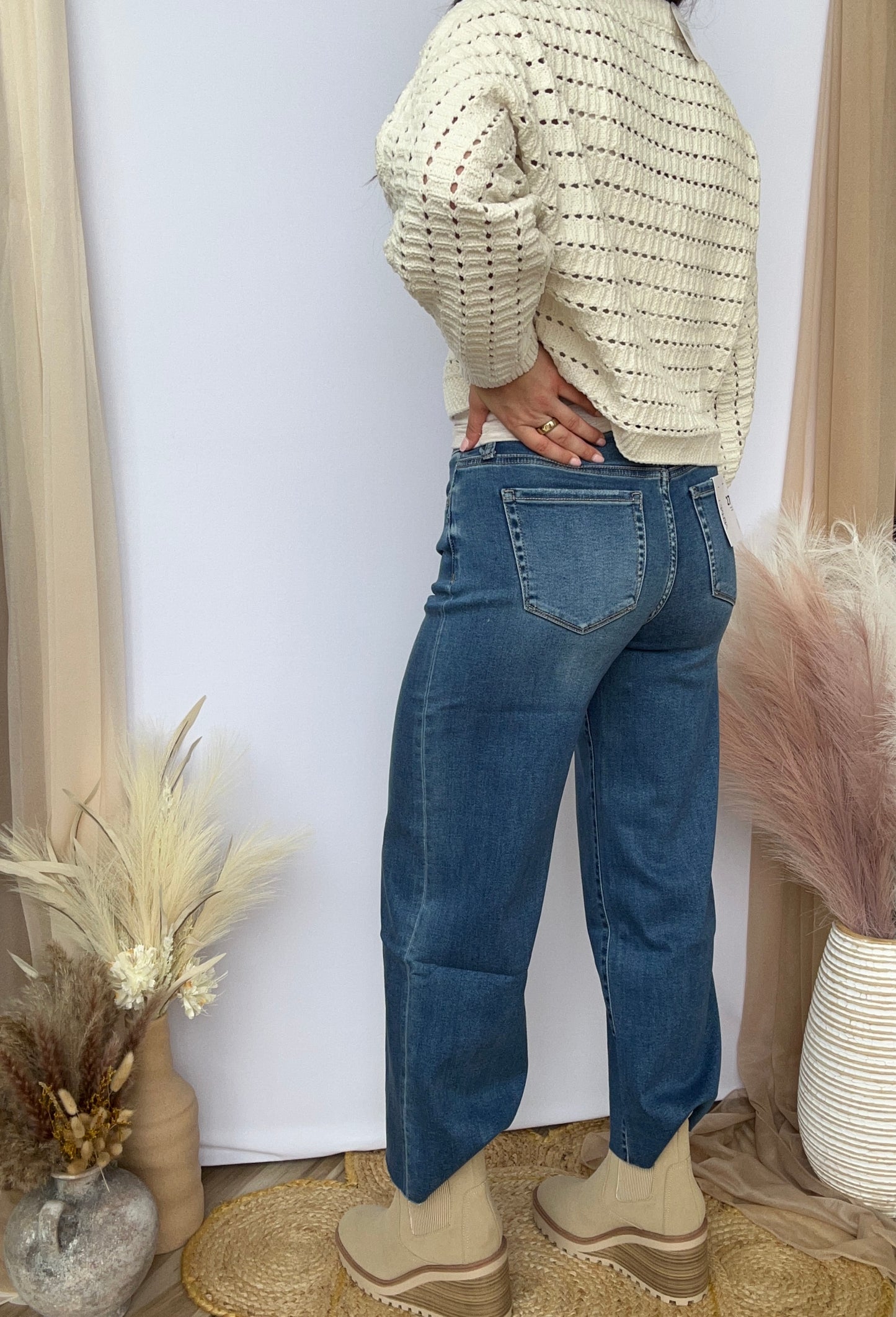 Person wearing blue jeans and a light-colored sweater standing against a white wall with decorative elements.