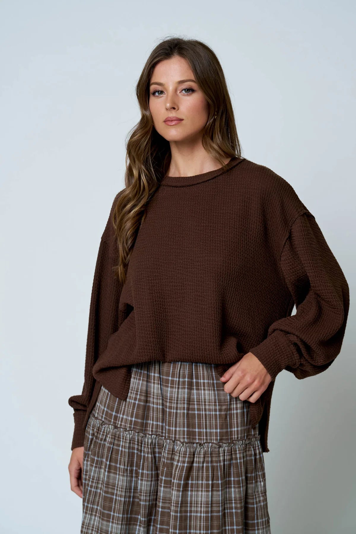 Woman wearing a brown sweater and plaid skirt against a light gray background