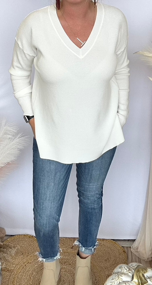 Person wearing a white sweater and blue jeans against a plain background