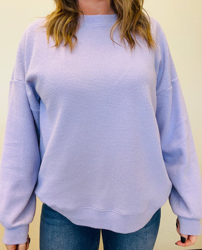 Person wearing a light purple textured sweater and blue jeans against a beige background