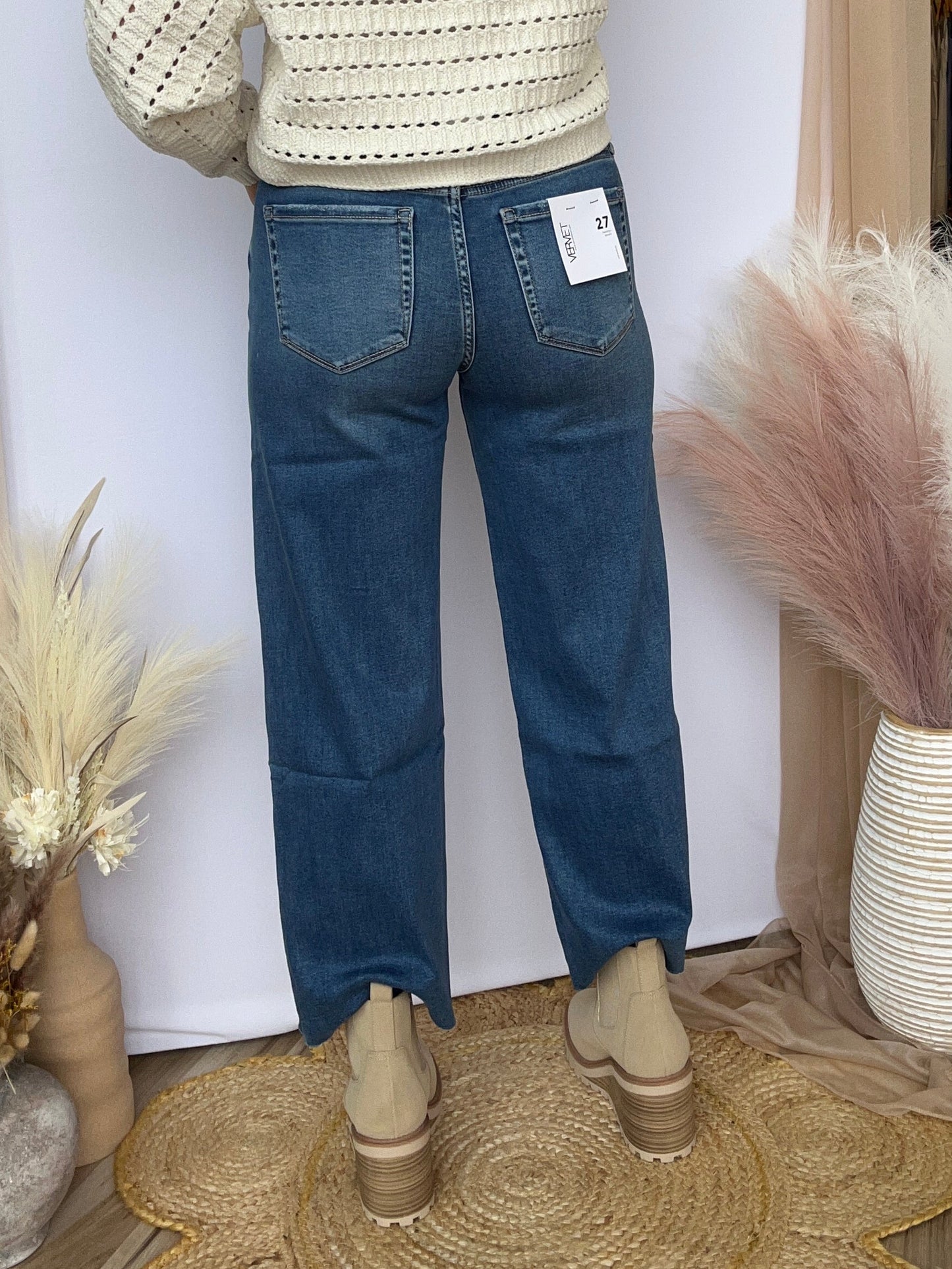 Mannequin wearing a cream sweater and blue jeans with decorative elements on a white surface.