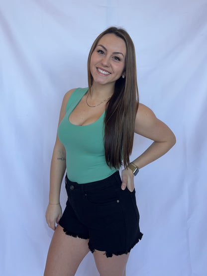 Woman wearing a green tank top and black shorts against a white background