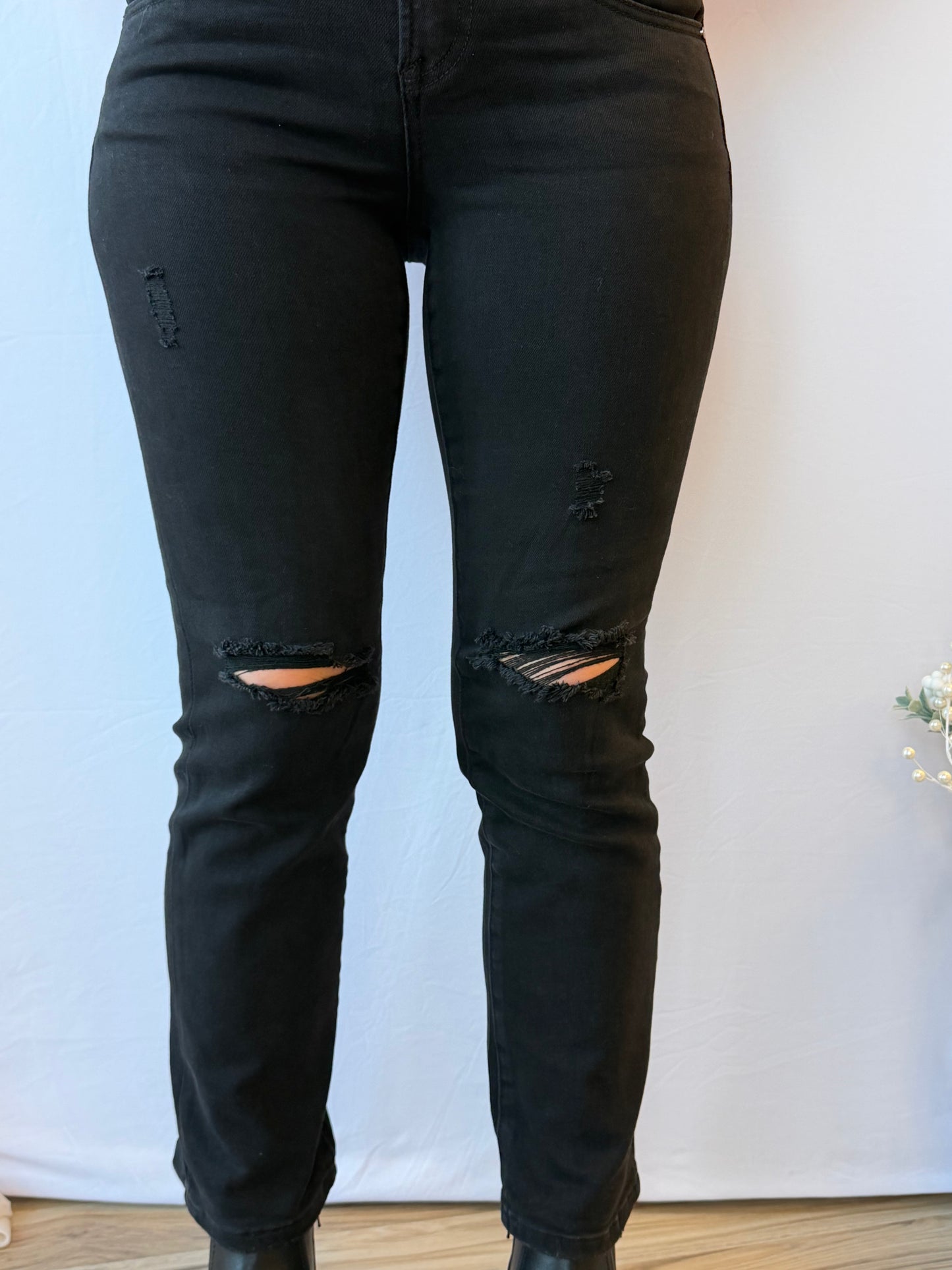 Black distressed jeans worn by a person on a light blue and white background