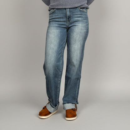 Person wearing blue jeans and brown shoes standing on a wooden floor.