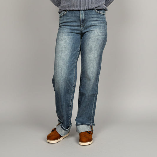 Person wearing blue jeans and brown shoes standing on a wooden floor.