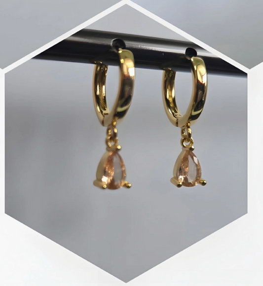 Three pairs of gold huggie hoop earrings with teardrop-shaped drop stones are displayed in a collage format. The top-left pair has a pink stone, the top-right pair has a green stone, and the bottom pair has a peach-colored stone, all shown hanging from black rods against a light gray background.